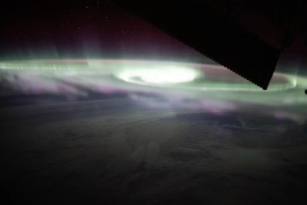 Aurora australis photographed from the International Space Station: a green band hugging the horizon, with magenta curtains rising above it into a starry sky.